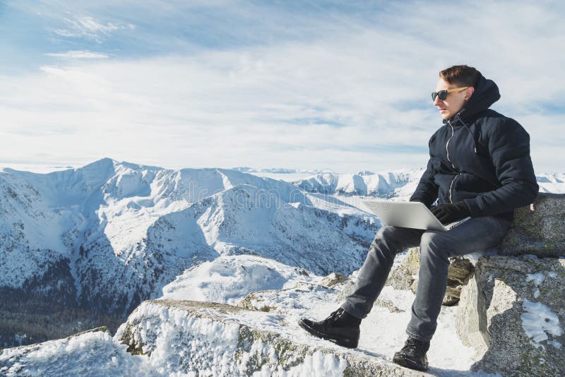 Young blogger or freelancer working on a laptop on top of the world. Winter lanscape in sunny day.