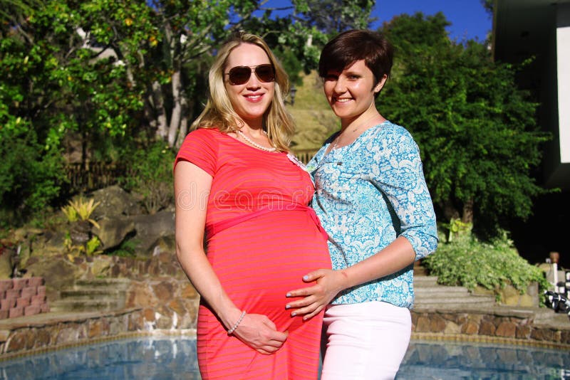 Young blond pregnant woman with her friend by the pool.