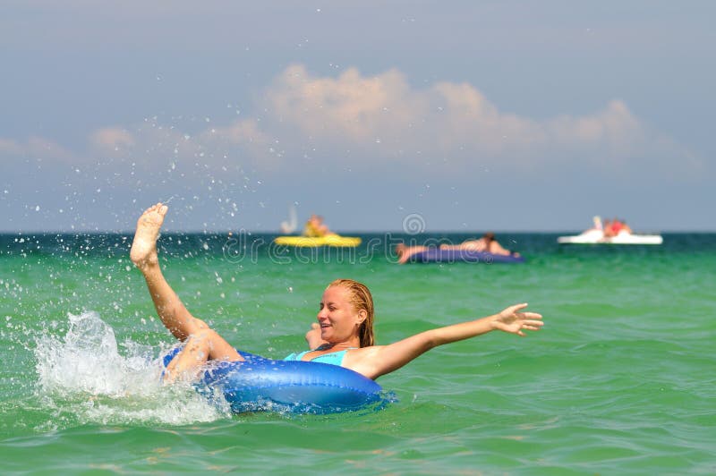 Young blond woman in blue bikini riding on swimming circle in sea and smiling