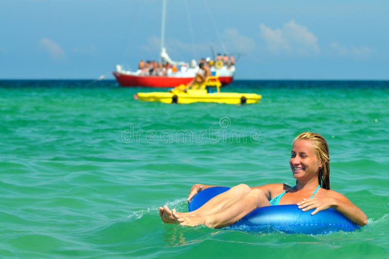 Young blond woman in blue bikini riding on swimming circle in sea and smiling