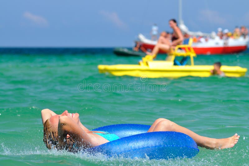 Young blond woman in blue bikini riding on swimming circle in sea and smiling