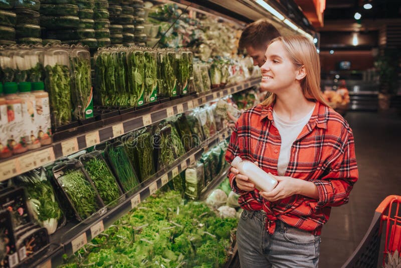 Young blonde cheerful woman in grocery store. She look at shelfs with different herbs and smile. Young woman nake a