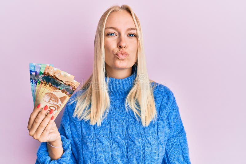 Young Blonde Girl Holding Canadian Dollars Looking at the Camera Blowing a Kiss on Air Being Lovely and Stock Photo