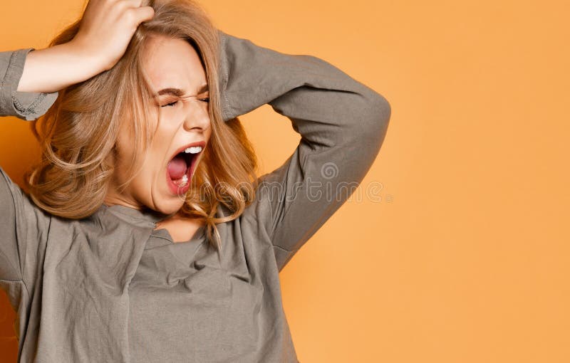 Young blonde girl in short blouse has got into a terrible situation. She tears her hair out and shouts loudly on yellow background. Young blonde girl in short blouse has got into a terrible situation. She tears her hair out and shouts loudly on yellow background