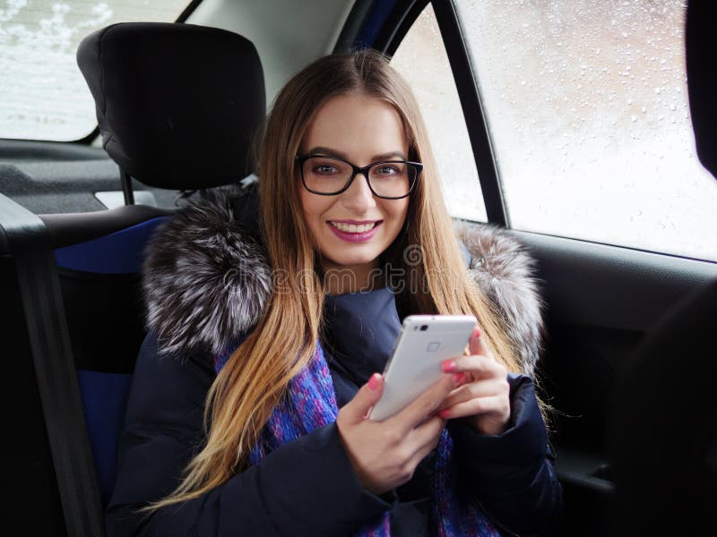 Young Blonde Woman In Glasses Using Smartphone On Back Seat In Car