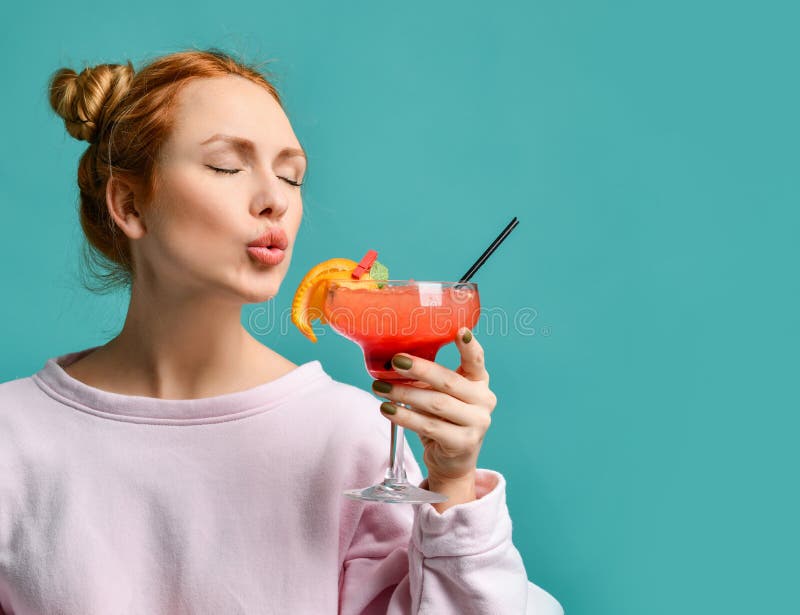 Young blonde woman with hairs in bun and closed eyes going to try a strawberry margarita cocktail