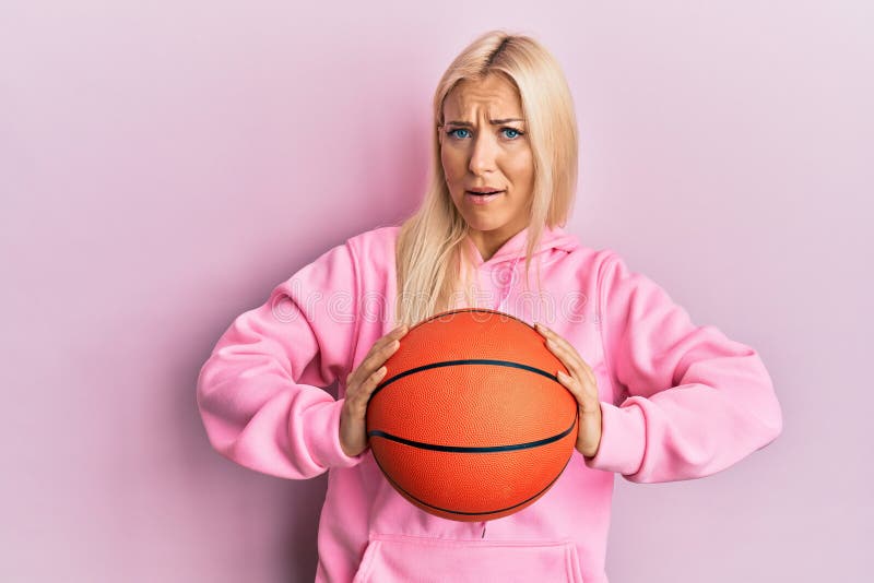 Young Blonde Woman Holding Basketball Ball Clueless And Confused