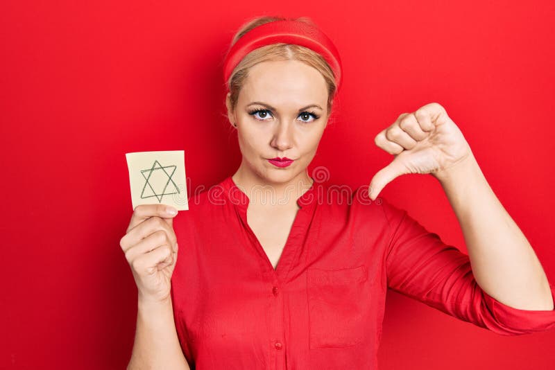Young blonde woman holding jew star reminder with angry face, negative sign showing dislike with thumbs down, rejection concept