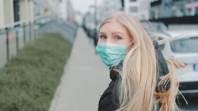 Young blonde woman in a medical mask escaping from somebody on the street. royalty free stock photography Young blonde woman in a medical mask escaping from somebody on the street. royalty free stock photography