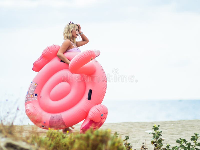 Young woman standing behind the inflatable flamingo on the beach