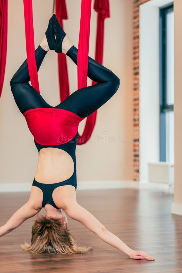 Blonde woman practices inversion anti-gravity yoga position, hanging upside down royalty free stock image