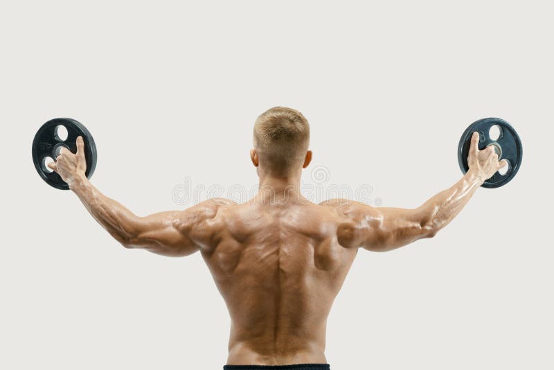 Studio shot of young bodybuilder lifting weights rising hands against white background. Fit and muscles sportsman exercising with barbell plate turning back. Rear view shot of shirtless fitness model flexing arms.