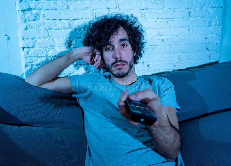 Portrait of bored sleepless young man sitting on the couch watching TV at night stock photo Portrait of bored sleepless young man sitting on the couch watching TV at night stock photo