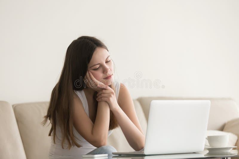 Young bored woman feeling drowsy at home sitting with laptop.