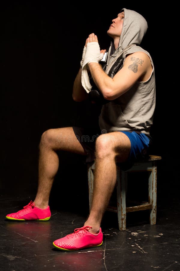 Young boxer praying for a win as he psyches himself up before a fight sitting on a stool with his hands clasped in prayer and eyes raised to heaven