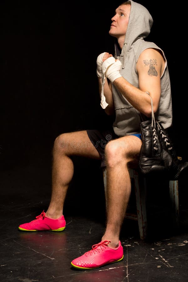 Young boxer psyching himself up before a match sitting on a stool with clasped hands looking up to the heavens for help in securing a victory.