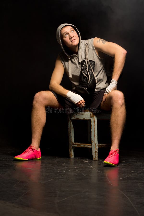 Young boxer seeking help from heaven sitting on a wooden stool with bandaged fists waiting for his match looking up beseechingly above his head hoping for a win.