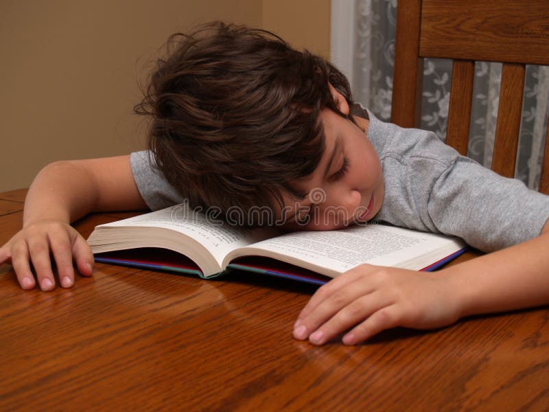 A young boy sitting at a table that fell asleep while reading a book. A young boy sitting at a table that fell asleep while reading a book.