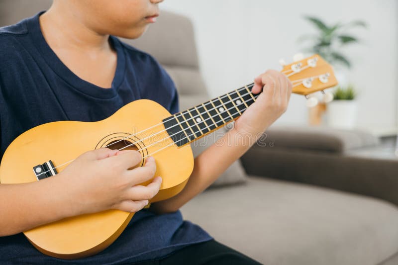 Young boy with a bright smile plays a ukulele on a gray couch. The cozy living royalty free stock photography