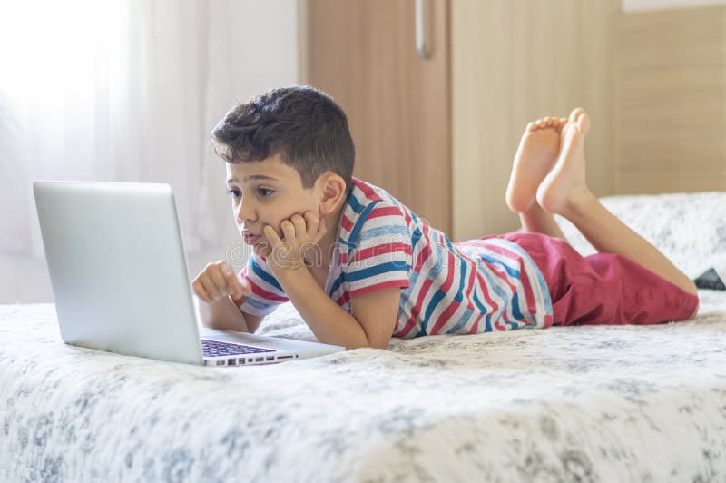 Young Boy Child Lying on Bed Using a Laptop. Online Class Lesson on