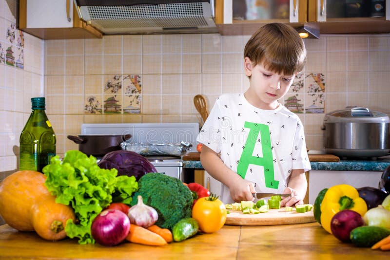 The Young Boy in Cooking Standing in the Kitchen Near Table with Stock