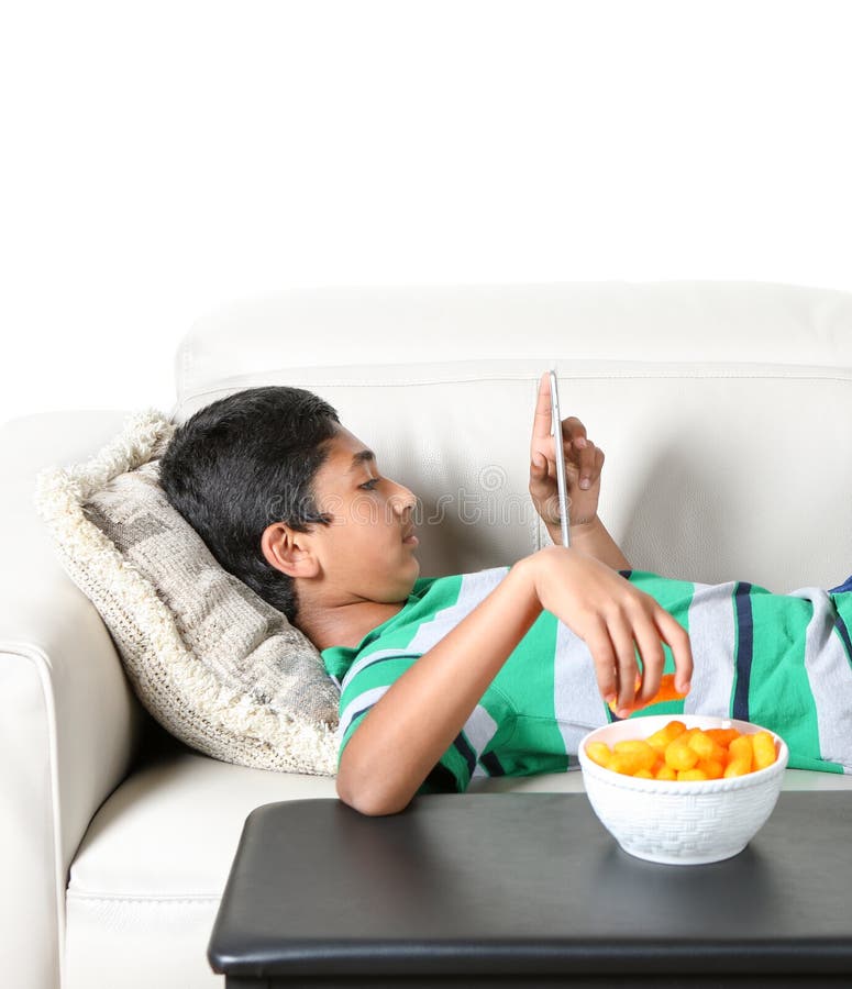 Young Boy on a Couch Staring into His Tablet and Eating Stock Photo