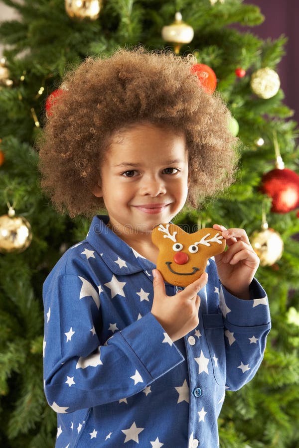 Young Boy Eating Cookie In Front Of Christmas Tree