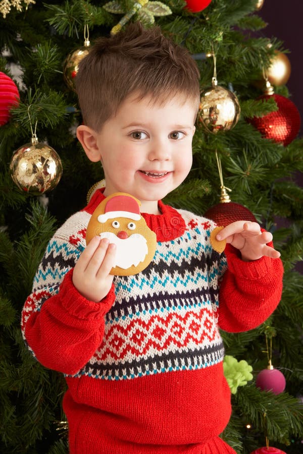 Young Boy Eating Cookie In Front Of Christmas Tree