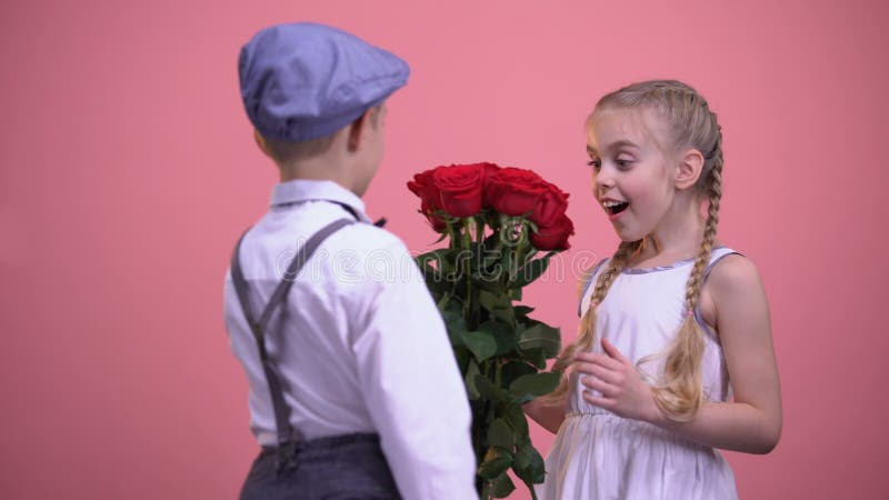 Young boy in formal clothes hiding roses behind back and presenting to girl