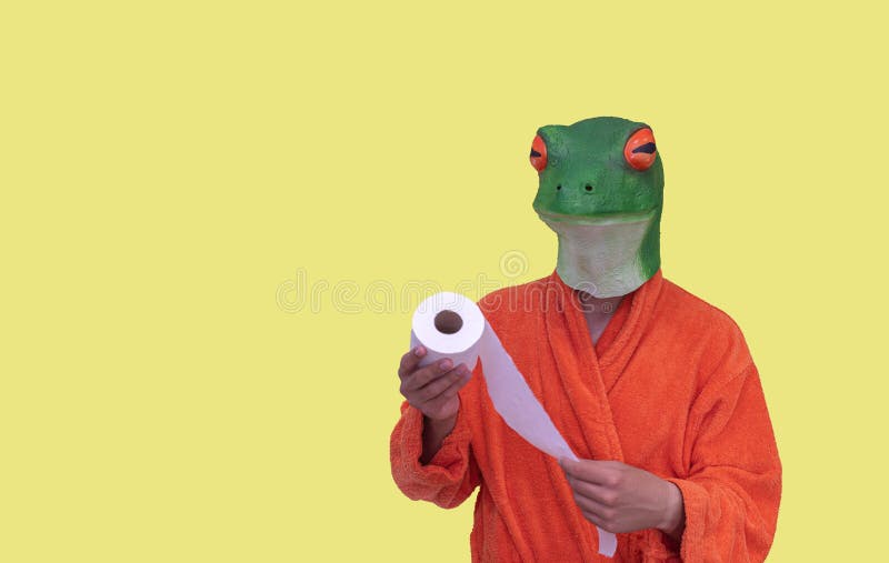 Young boy with a green frog animal mask in an orange bathrobe with a white toilet paper roll on a yellow background with copy