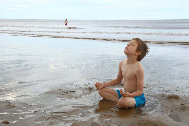 Un bambino con una giornata sulla spiaggia, un ragazzino di riposo sulla sabbia bagnata dal mare, in posizione yoga del loto.