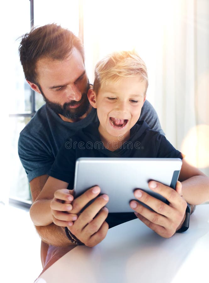 Young boy sitting with father at the table and using pc tablet in modern loft. Vertical, blurred background. Sunlights effect. stock photos Young boy sitting with father at the table and using pc tablet in modern loft. Vertical, blurred background. Sunlights effect. stock photos