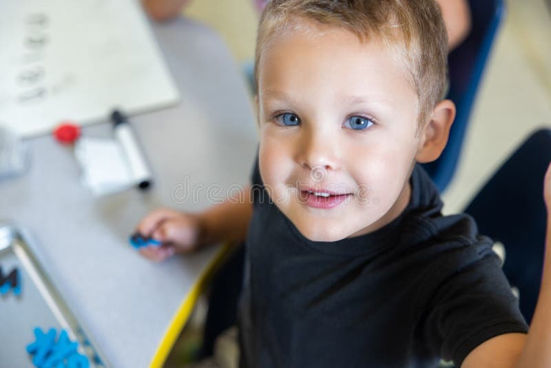 A young boy is sitting at a table with a white board behind him stock photo