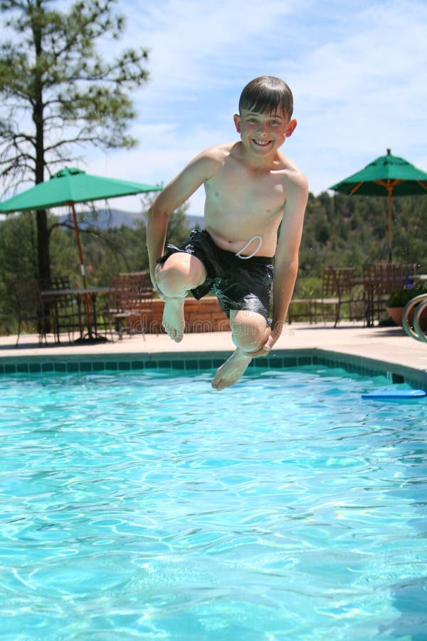 Young boy smiling and jumping into a swimming pool