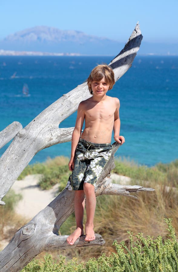 Junge, gesunde junge stehend im alten Baum an einem sonnigen Strand im Urlaub mit Mittelmeer und Afrika im hintergrund.