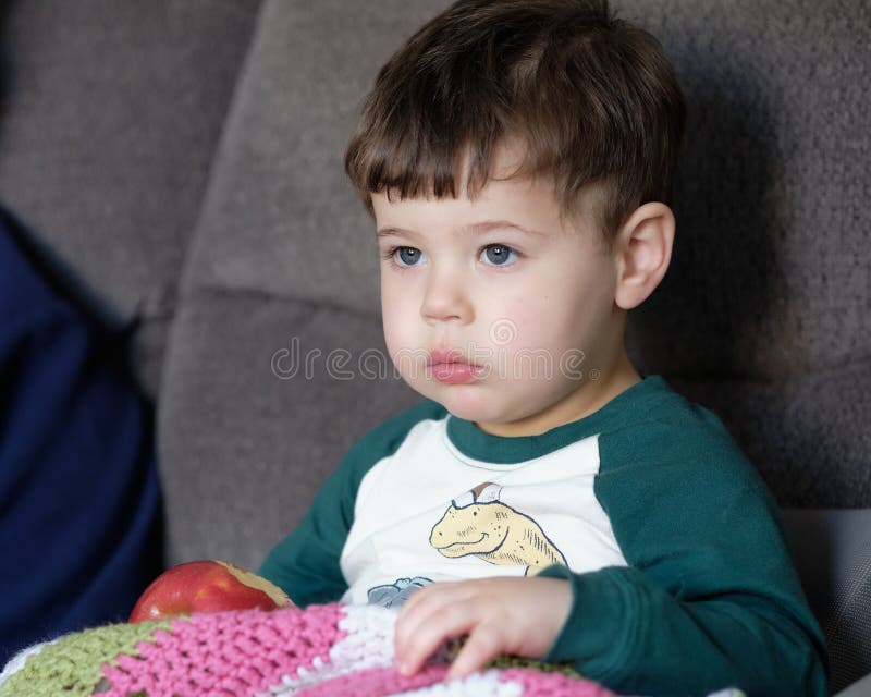 Young Boy Toddler is Eating an Apple on the Couch at Home Stock Image
