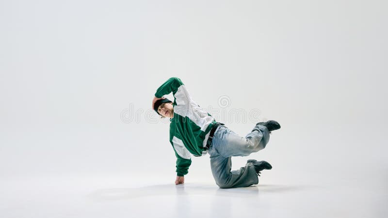 Young breakdancer, dressed vintage attire, balancing on one hand while body arches in dynamic pose against white studio royalty free stock images