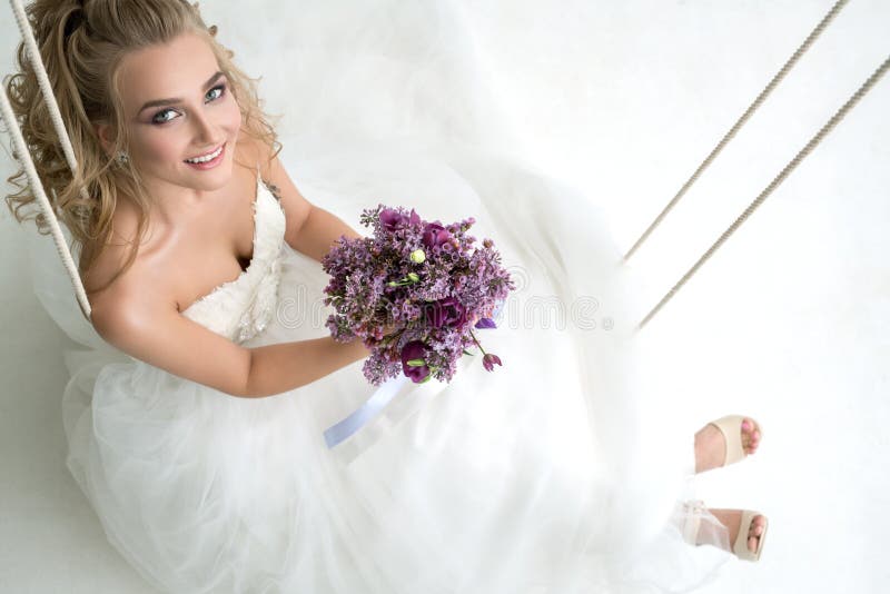 Young bride in studio on swing with fine bouquet