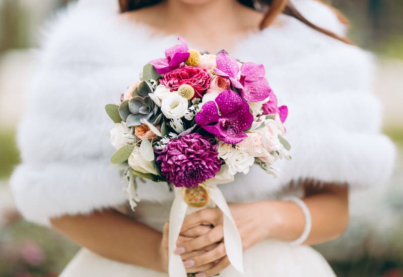 Giovane sposa nel giorno delle nozze holding bouquet contro sfondo sfocato.
