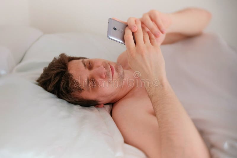 Young brunet handsome man wakes up, and check the time on his mobile phone. royalty free stock photo Young brunet handsome man wakes up, and check the time on his mobile phone. royalty free stock photo