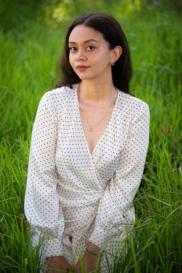 Young Brunette Female in a White Dress Kneeling in a Green Field of Young Brunette Female in a White Dress Kneeling in a Green Field of