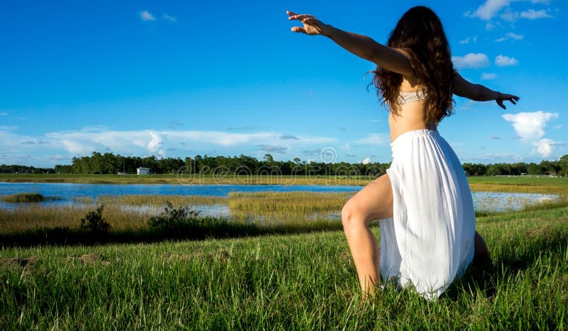 Young brunette spanish woman doing warrior 2 yoga pose in a field next to a lake with long curly hair royalty free stock photos Young brunette spanish woman doing warrior 2 yoga pose in a field next to a lake with long curly hair royalty free stock photos
