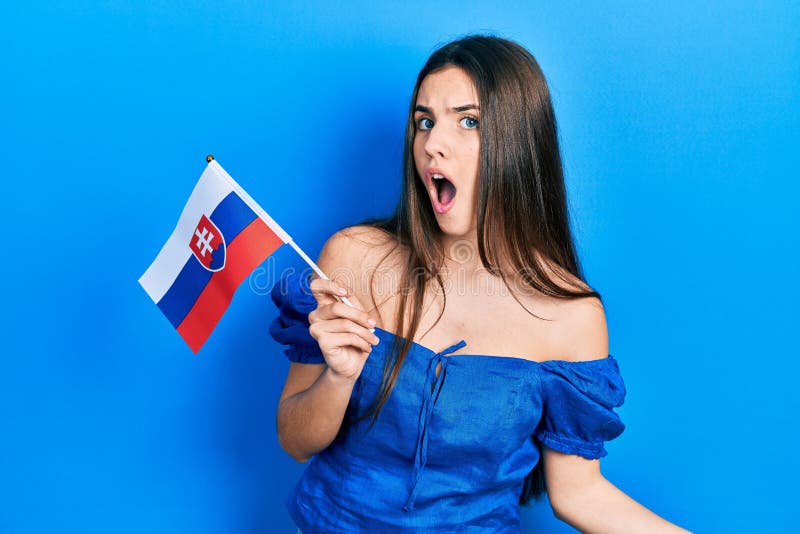 Mladá brunetka teenager drží vlajku slovenska vystrašený žasnutý s otvorenými ústami na prekvapenie, neveriacky tvár