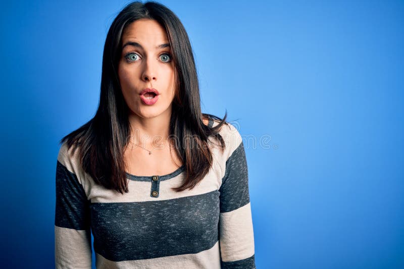 Young brunette woman with blue eyes wearing casual striped t-shirt standing over background afraid and shocked with surprise