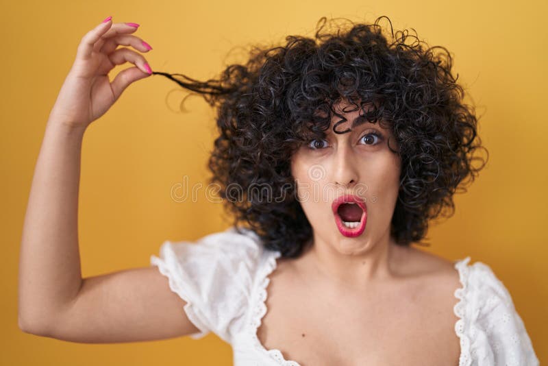 Young Brunette Woman With Curly Hair Holding Curl In Shock Face Looking Skeptical And Sarcastic