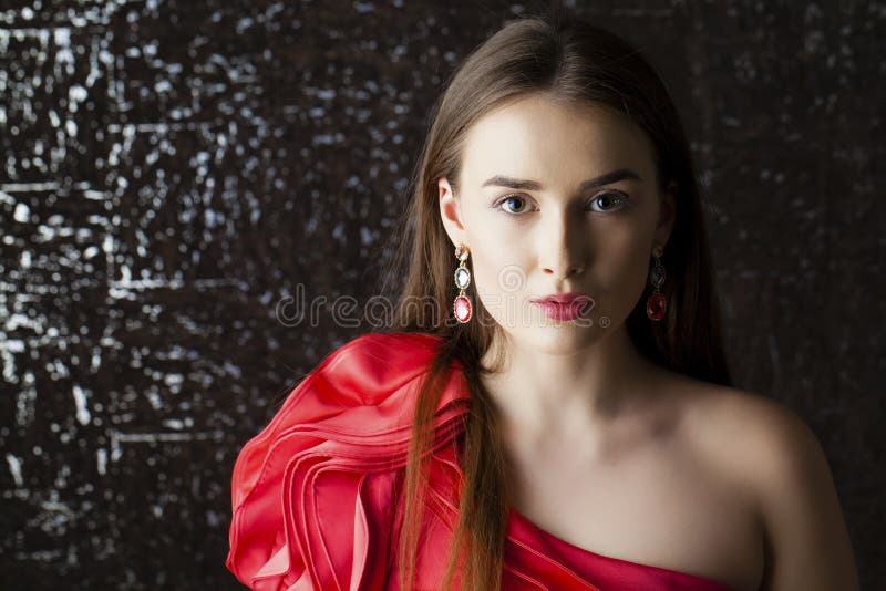 Young brunette woman on dark studio wall background. Dress, brown.