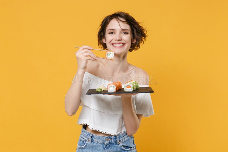 Young brunette woman girl in casual clothes hold in hand makizushi sushi roll served on black plate traditional japanese royalty free stock photography