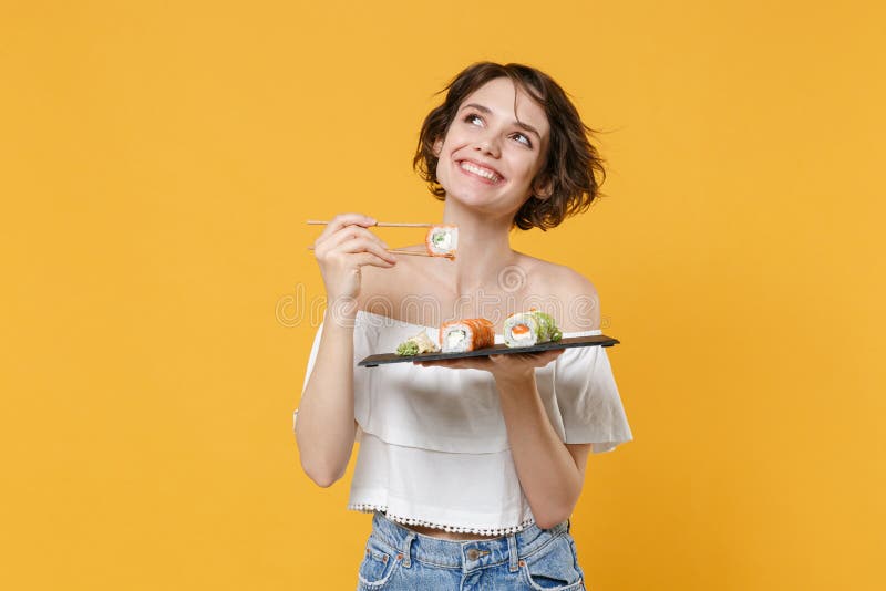 Young brunette woman girl in casual clothes hold in hand makizushi sushi roll served on black plate traditional japanese stock images