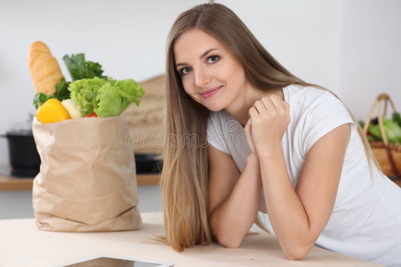 Young Brunette Woman Smiling While Sitting At The Table Near Paper Bag Full Of Vegetables And Fruits. Concept Of Foo