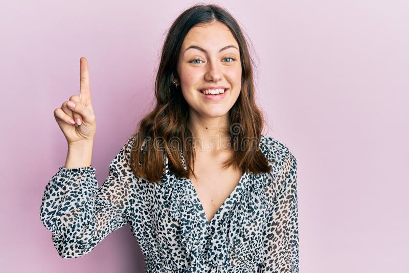 Young brunette woman wearing elegant animal print shirt smiling with an idea or question pointing finger up with happy face